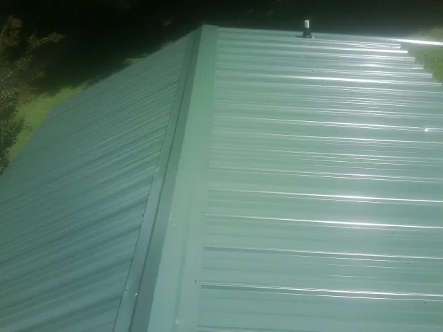 New green metal panels meeting at the ridge of a roof — Flat Roof Repair work by our crew in Newcastle